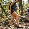 Mujer con sandalias Sowilo Raido negras caminando en sendero de bosque.